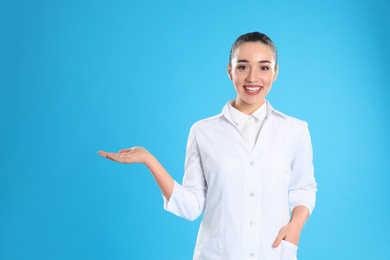Photo of Happy young woman in lab coat on light blue background
