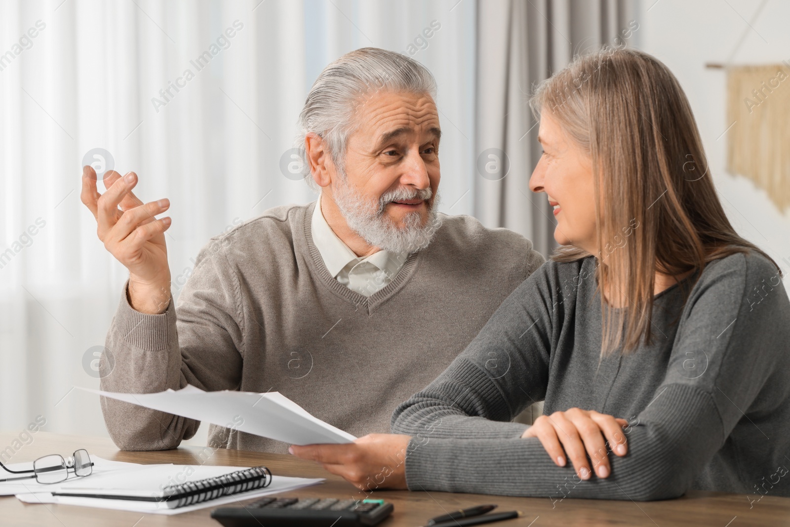 Photo of Elderly couple with papers discussing pension plan at wooden table indoors