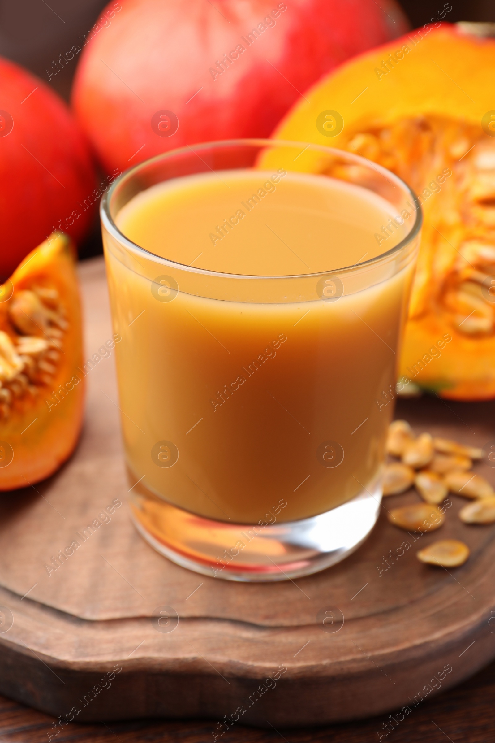 Photo of Tasty pumpkin juice in glass, whole and cut pumpkins on wooden table, closeup