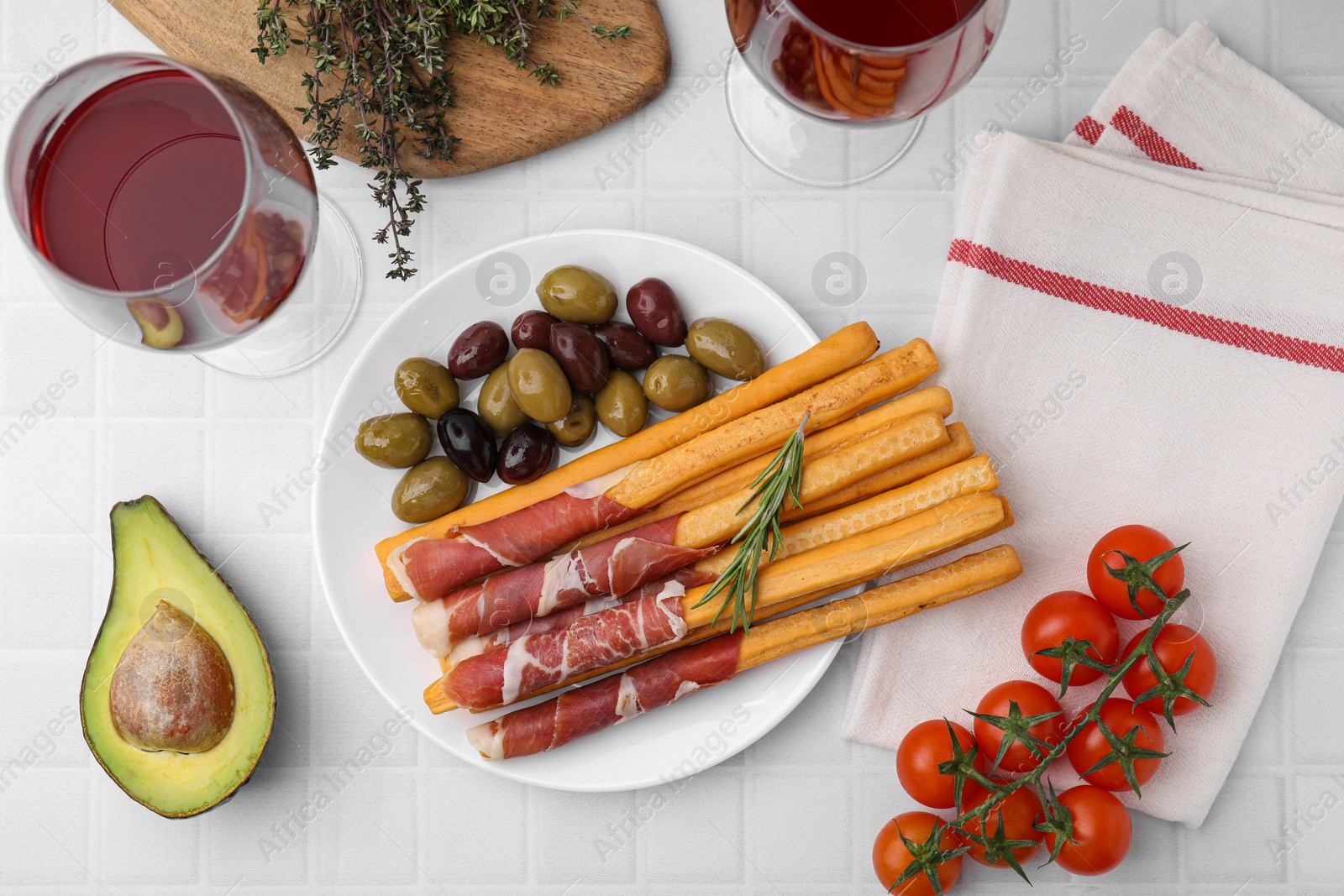 Photo of Delicious grissini sticks with prosciutto and ingredients on white table, flat lay