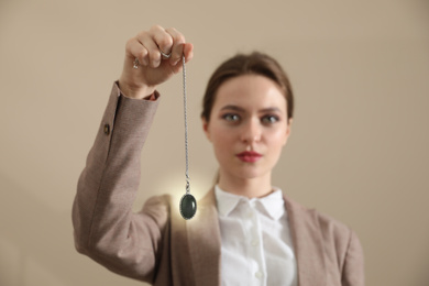 Photo of Psychotherapist with pendulum on beige background. Hypnotherapy session