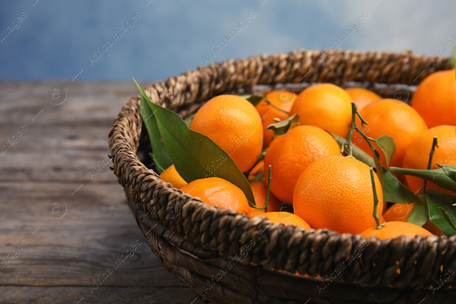 Photo of Fresh ripe tangerines in wicker basket on wooden table