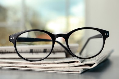 Stack of newspapers and glasses on grey table indoors, closeup