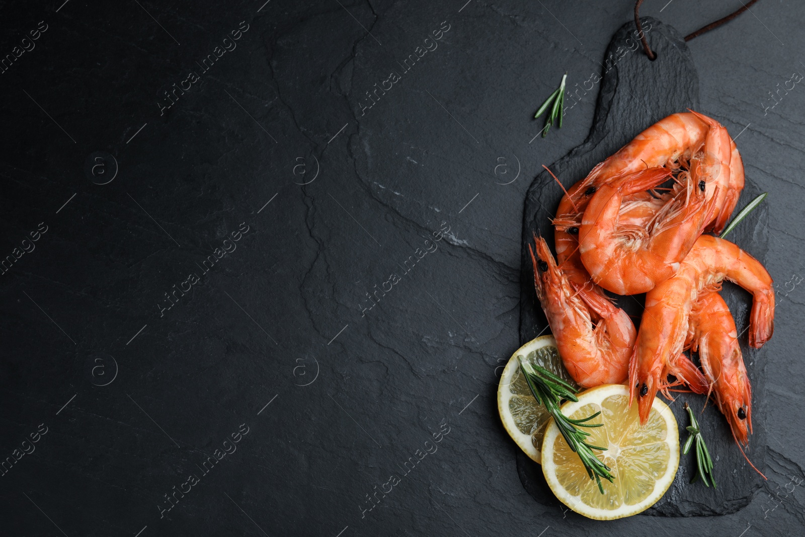 Photo of Delicious cooked shrimps with lemon and rosemary on black table, flat lay. Space for text