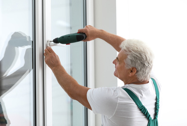 Photo of Mature construction worker repairing plastic window with electric screwdriver indoors