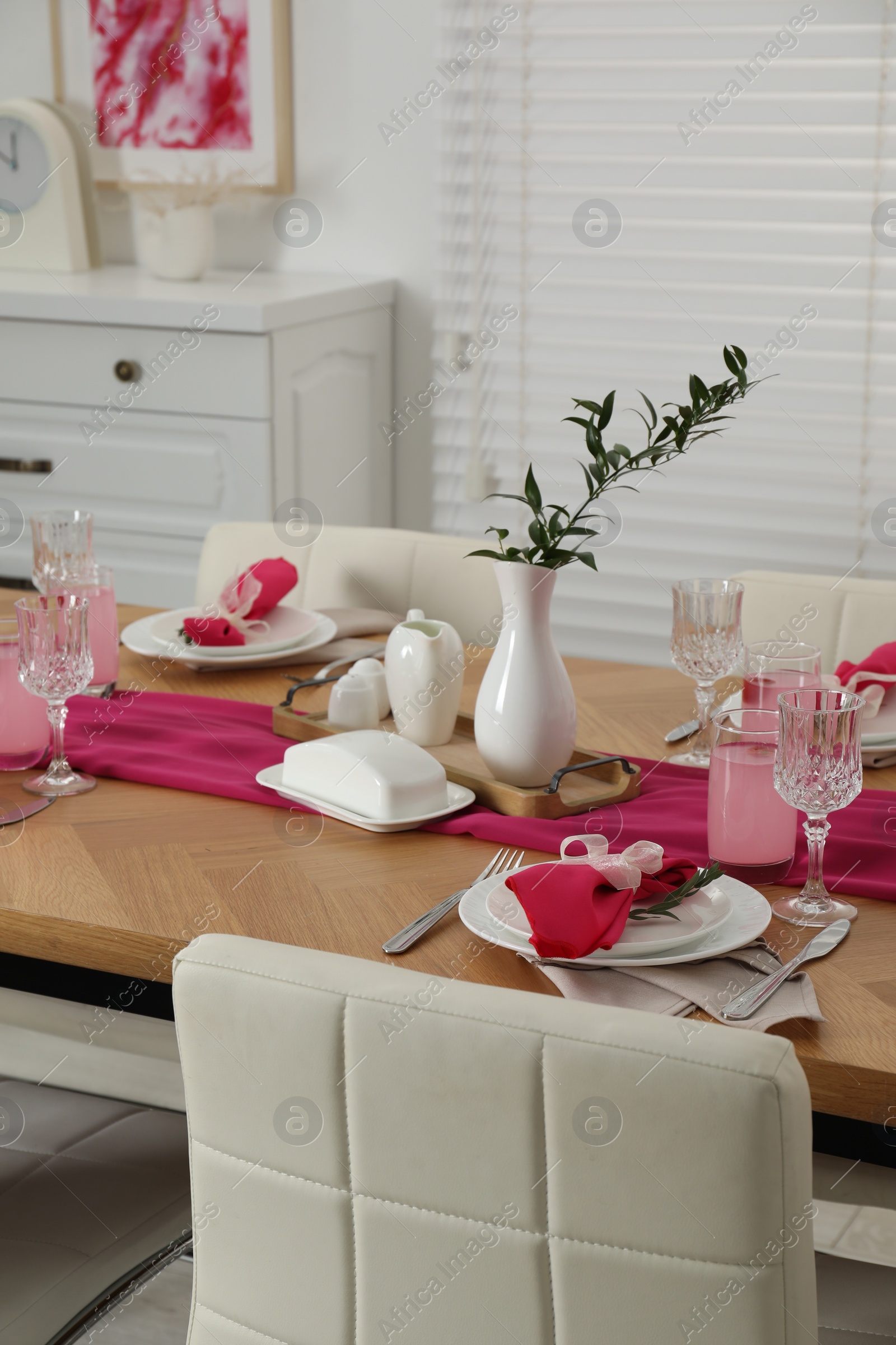 Photo of Color accent table setting. Glasses, plates, pink napkins and vase with green branch in dining room