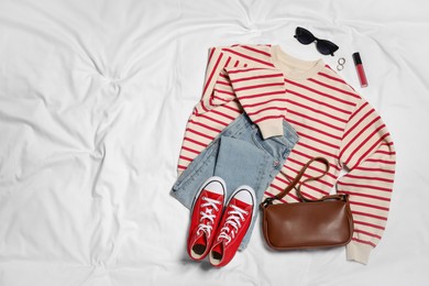 Photo of Pair of stylish red sneakers, clothes and accessories on white fabric, flat lay. Space for text