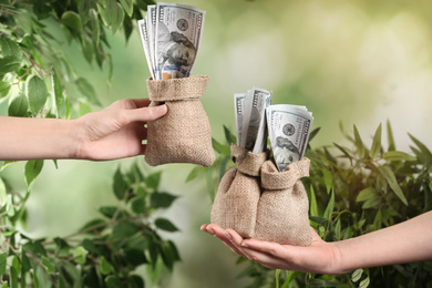 People holding sacks with dollar bills on blurred background, closeup. Money transfer