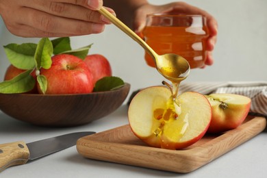 Woman pouring sweet honey onto fresh apple at white table, closeup