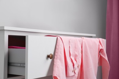 Pink shirt on white chest of drawers indoors, closeup