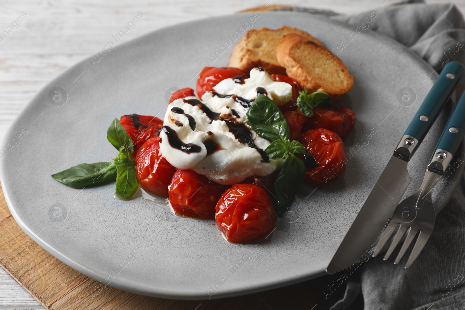 Photo of Delicious burrata cheese served with tomatoes, croutons and basil sauce on white wooden table, closeup