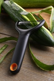 Photo of Fresh cucumber, peels and peeler on wooden table, closeup