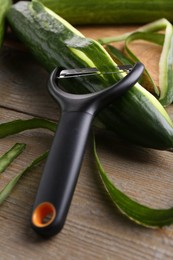 Fresh cucumber, peels and peeler on wooden table, closeup