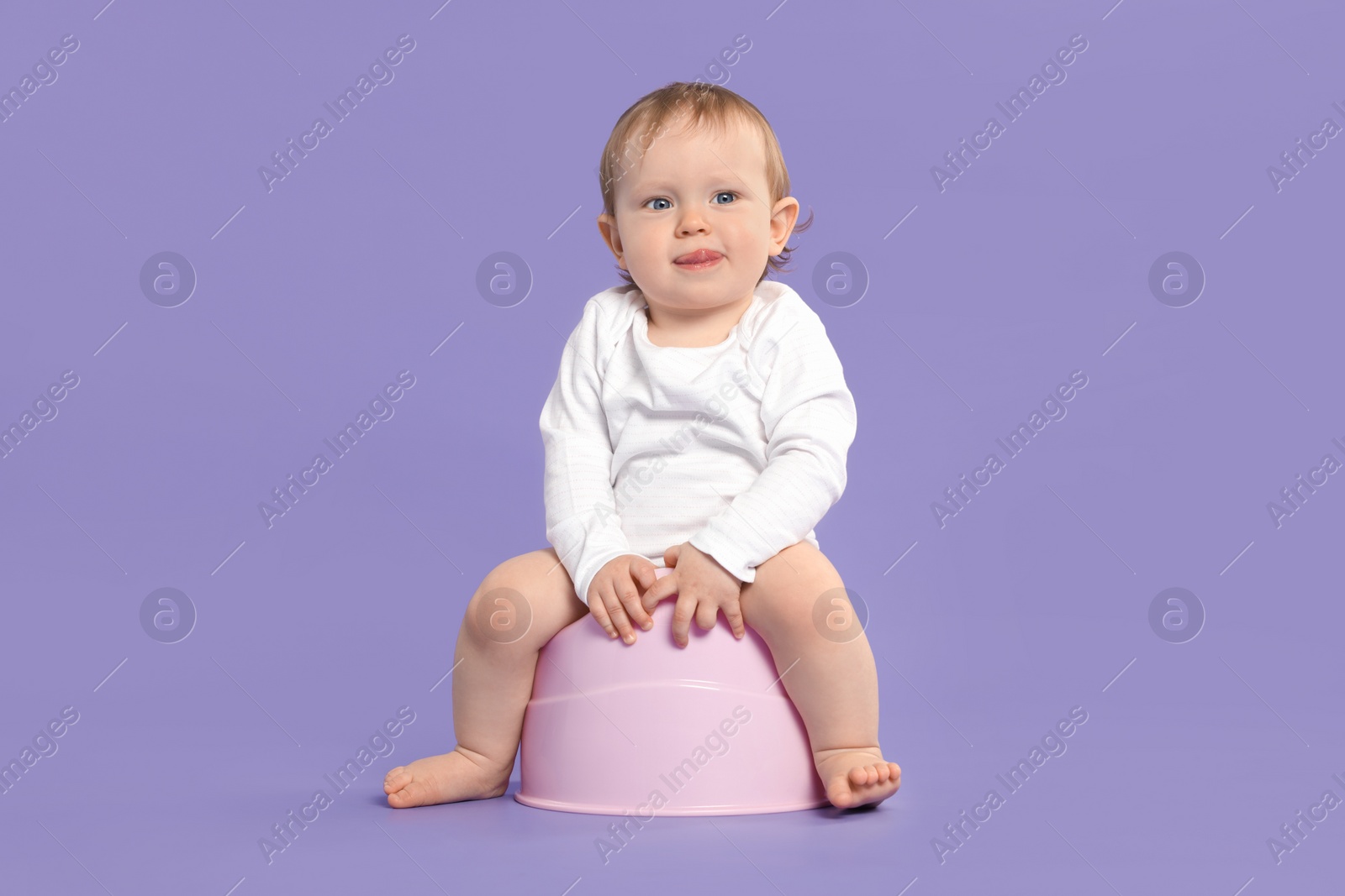 Photo of Little child sitting on baby potty against violet background