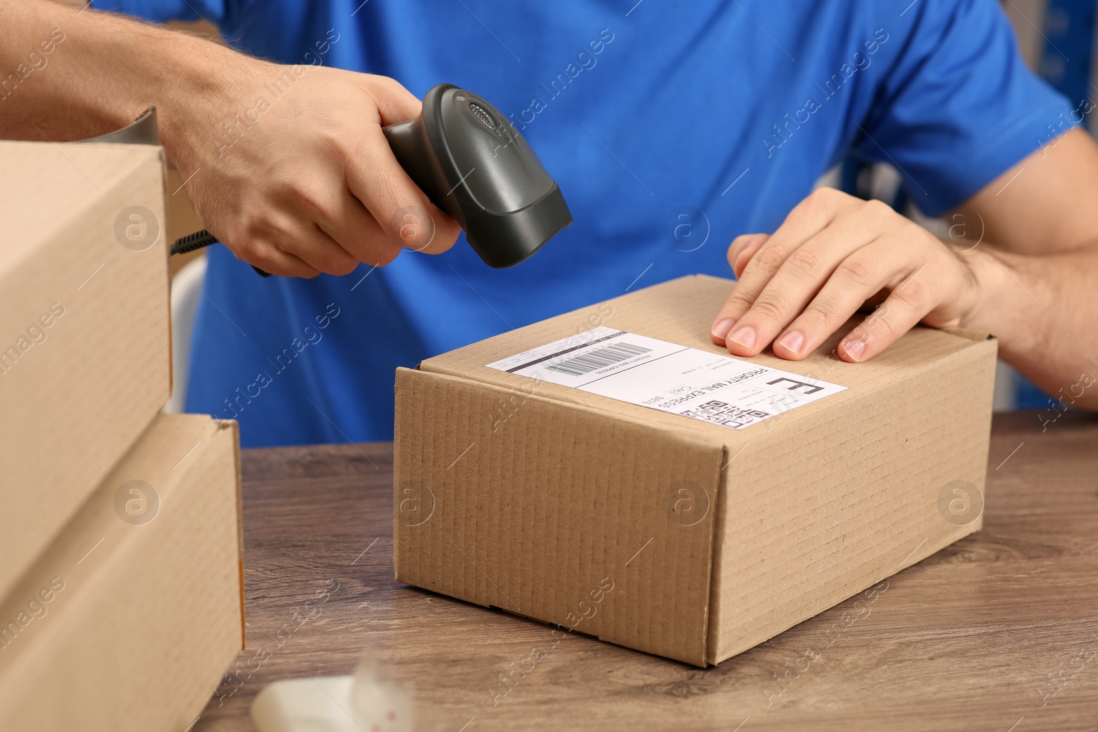 Photo of Post office worker with scanner reading parcel barcode at counter, closeup