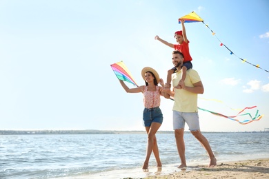 Photo of Happy parents and their child playing with kites on beach near sea. Spending time in nature