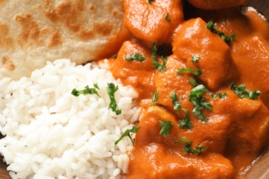 Delicious butter chicken with rice and naan as background, closeup