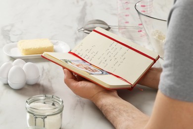 Photo of Man with recipe book at white marble table in kitchen, closeup