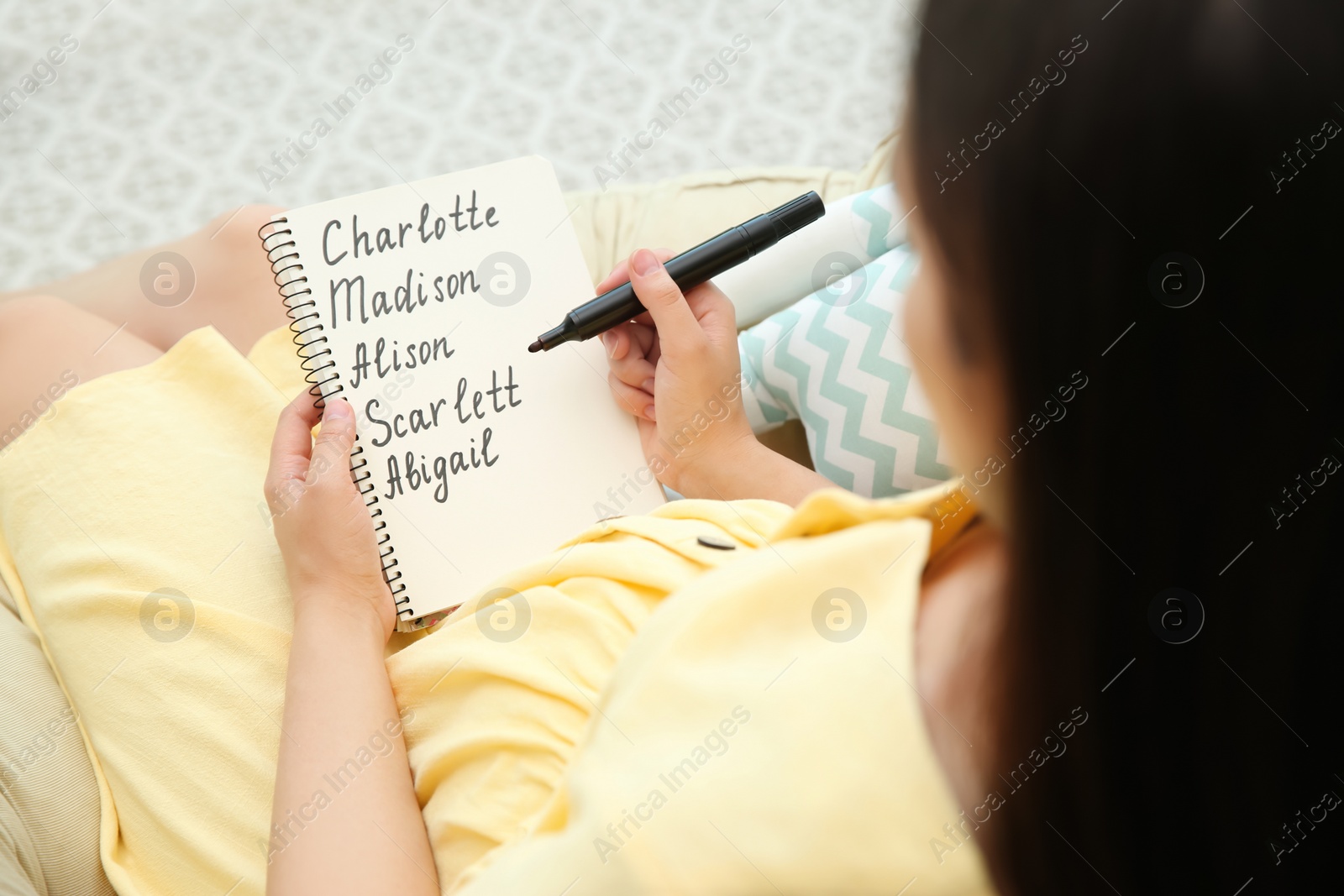 Photo of Pregnant woman with baby names list sitting in armchair, closeup