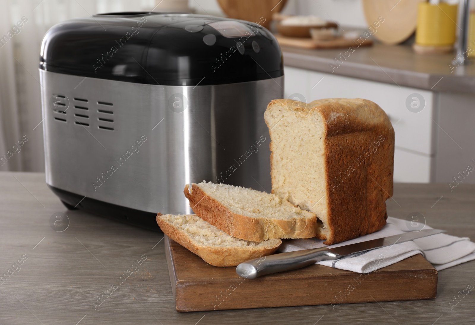 Photo of Breadmaker and cut homemade bread on wooden table in kitchen