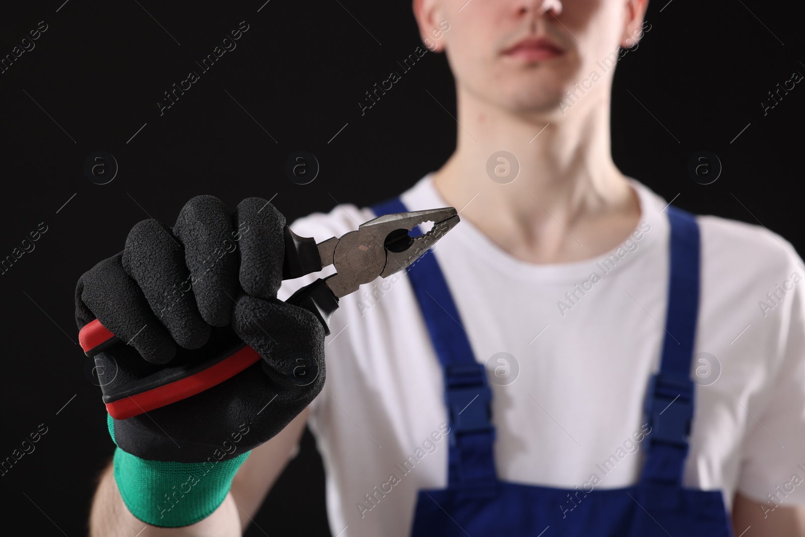 Photo of Young man holding pliers on black background, closeup