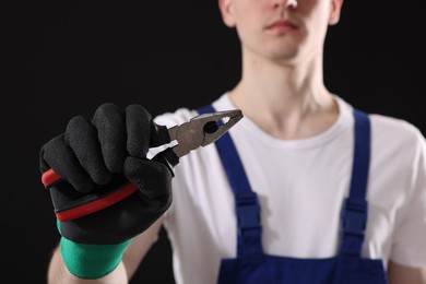 Photo of Young man holding pliers on black background, closeup