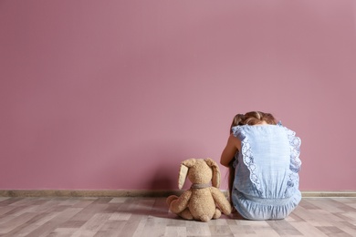 Photo of Little girl with toy sitting on floor near color wall in empty room. Autism concept