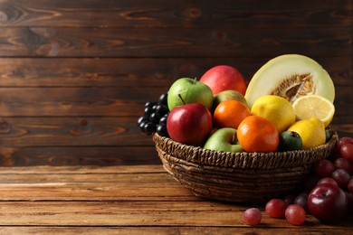 Different ripe fruits in wicker basket on wooden table, space for text