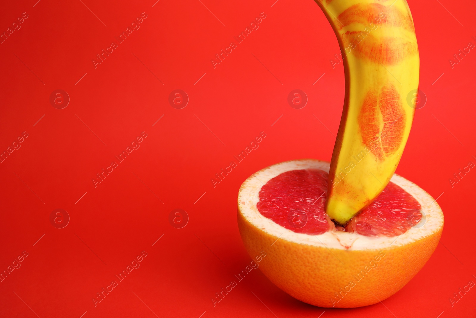 Photo of Fresh grapefruit and banana with lipstick marks on red background, space for text. Sex concept