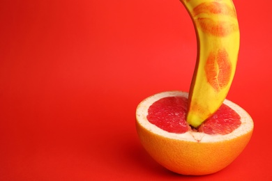 Photo of Fresh grapefruit and banana with lipstick marks on red background, space for text. Sex concept