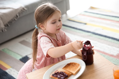 Photo of Little girl with jam and toasts in living room