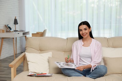 Photo of Young woman coloring antistress page on sofa in living room