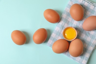 Photo of Cracked and whole chicken eggs with napkin on light blue background, flat lay