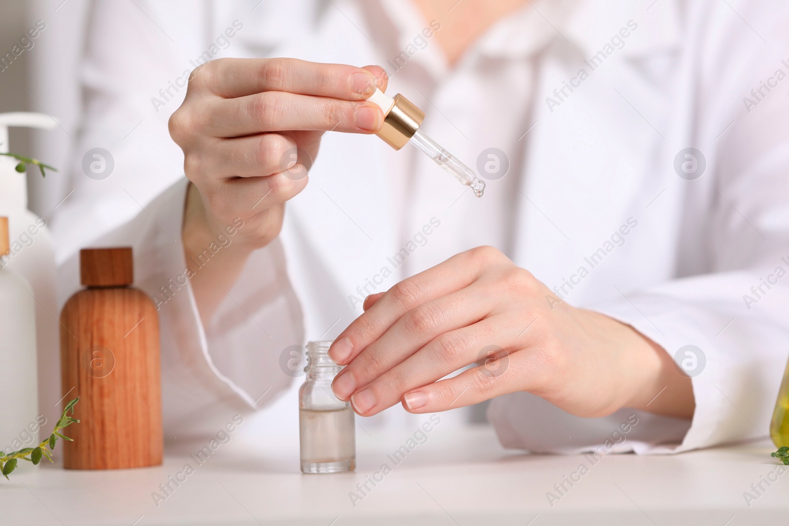 Photo of Dermatologist testing essential oil at white table indoors, selective focus