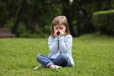 Photo of Little girl suffering from seasonal spring allergy on green grass in park