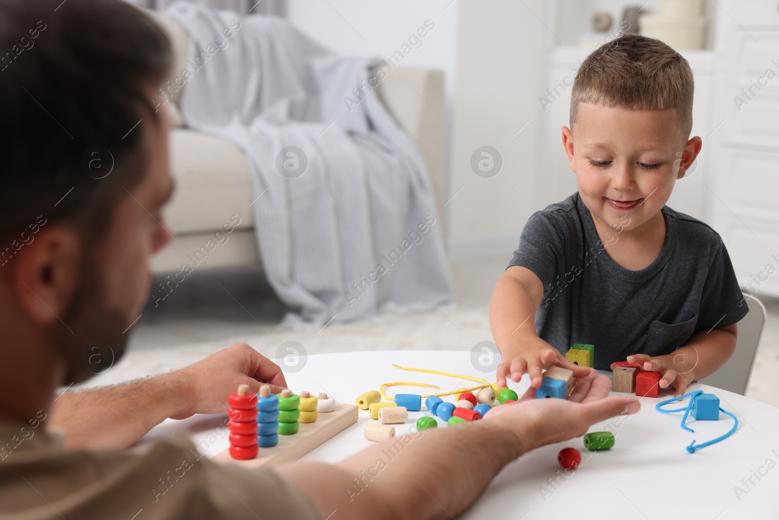 Photo of Motor skills development. Father and his son playing with wooden pieces at table indoors