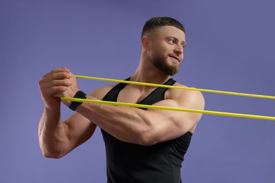 Photo of Muscular man exercising with elastic resistance band on purple background