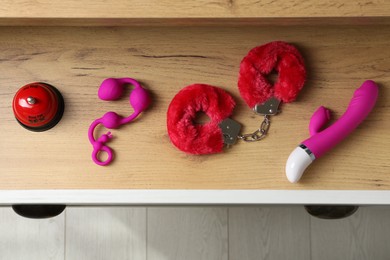 Photo of Different modern sex toys in open wooden drawer, top view