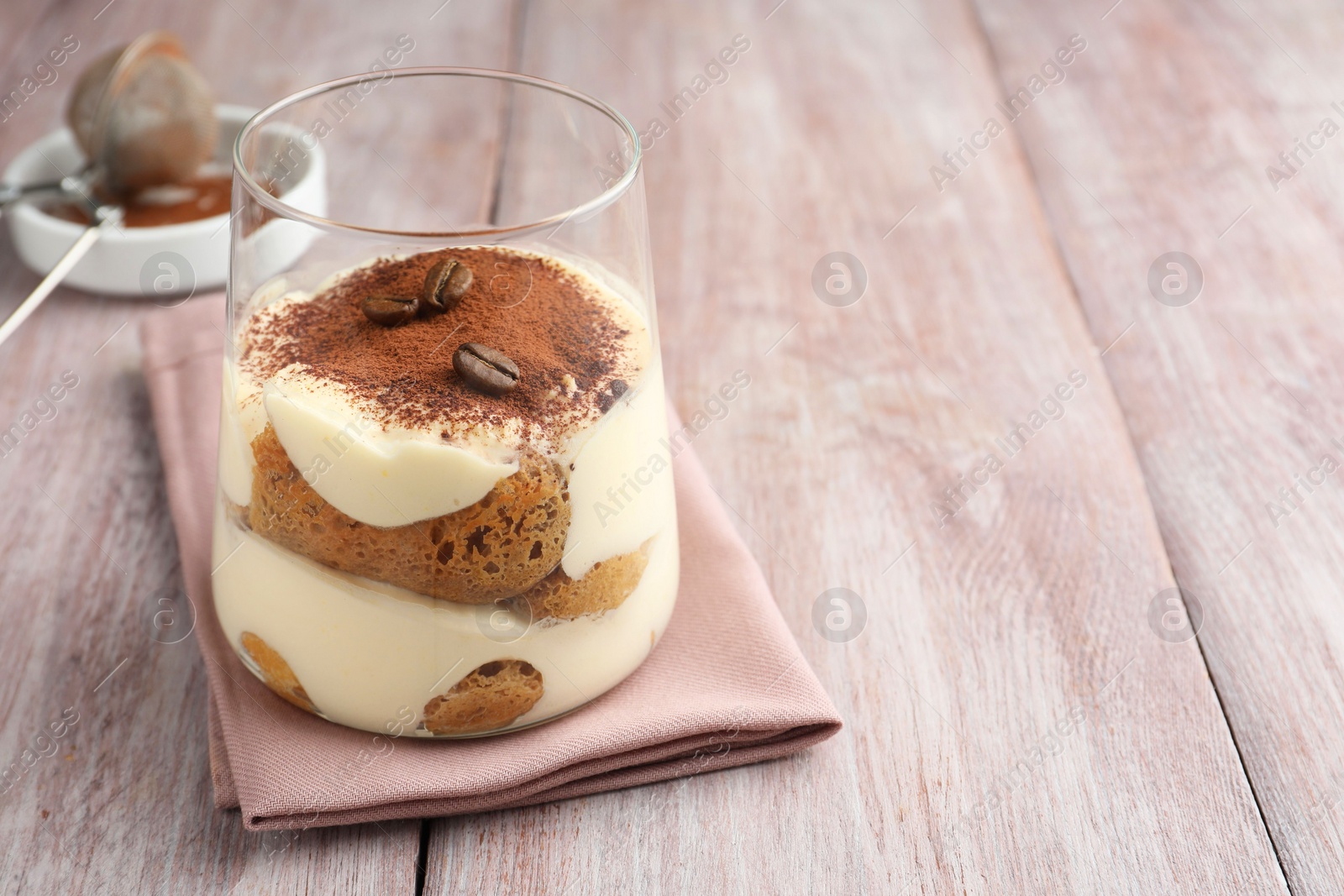 Photo of Delicious tiramisu with coffee beans in glass on wooden table, space for text