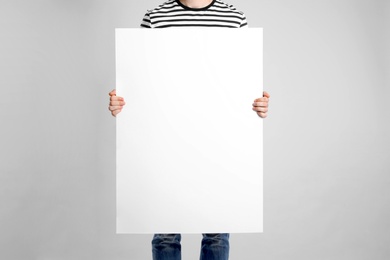 Photo of Man holding blank poster on light grey background, closeup