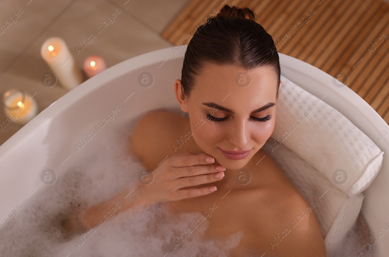 Photo of Young woman using pillow while enjoying bubble bath indoors, above view