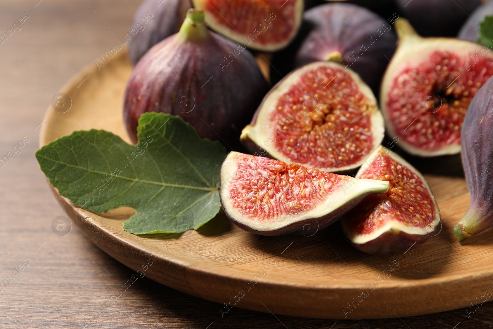 Photo of Whole and cut ripe figs with leaf on wooden table, closeup