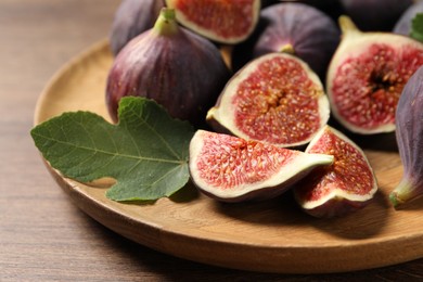 Photo of Whole and cut ripe figs with leaf on wooden table, closeup