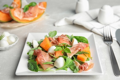 Photo of Fresh melon with prosciutto, mozzarella and arugula on table