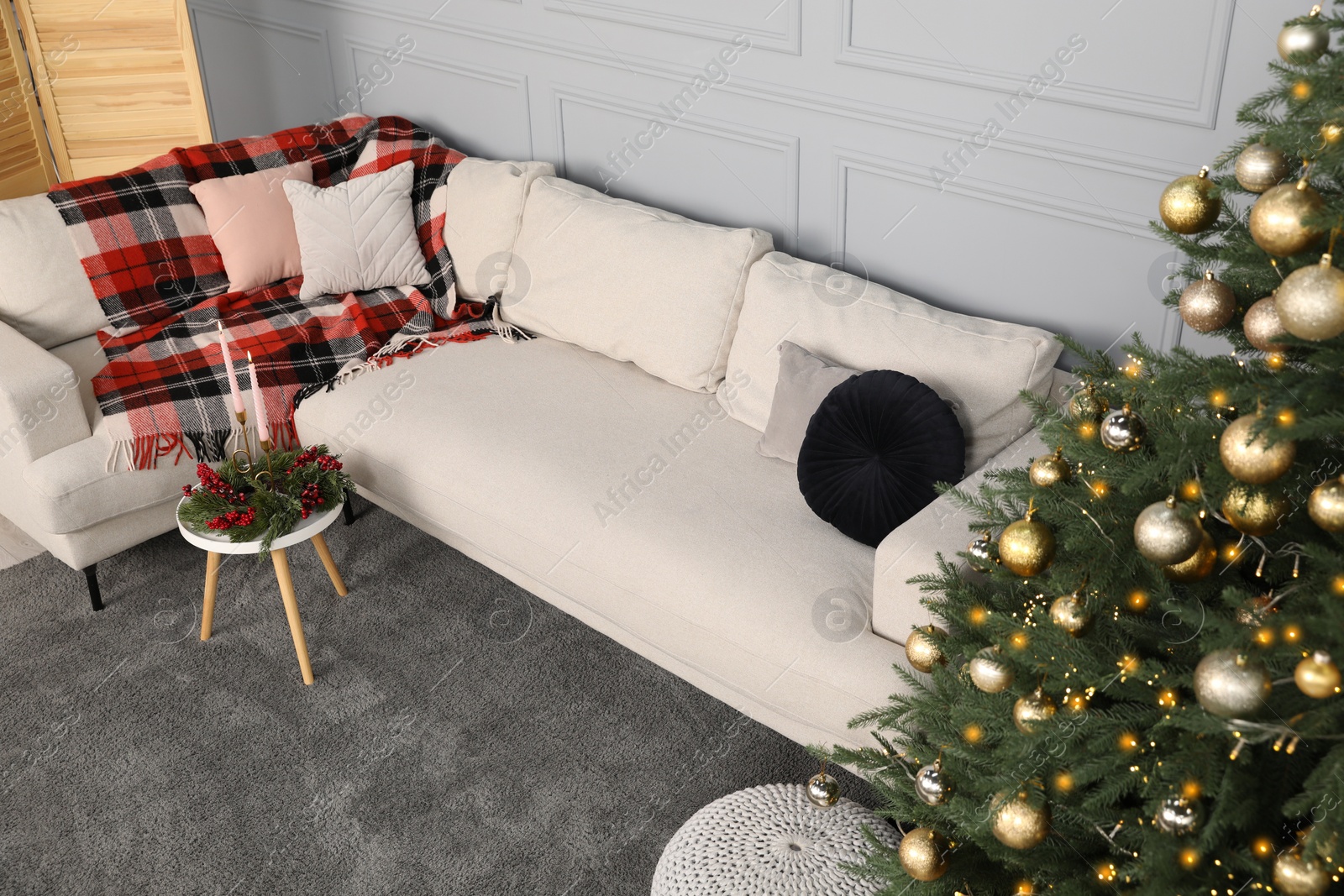 Photo of Beautiful Christmas tree, sofa and candles on table in living room