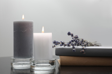 Wax candles in glass holders near books and lavender flowers on table against light background