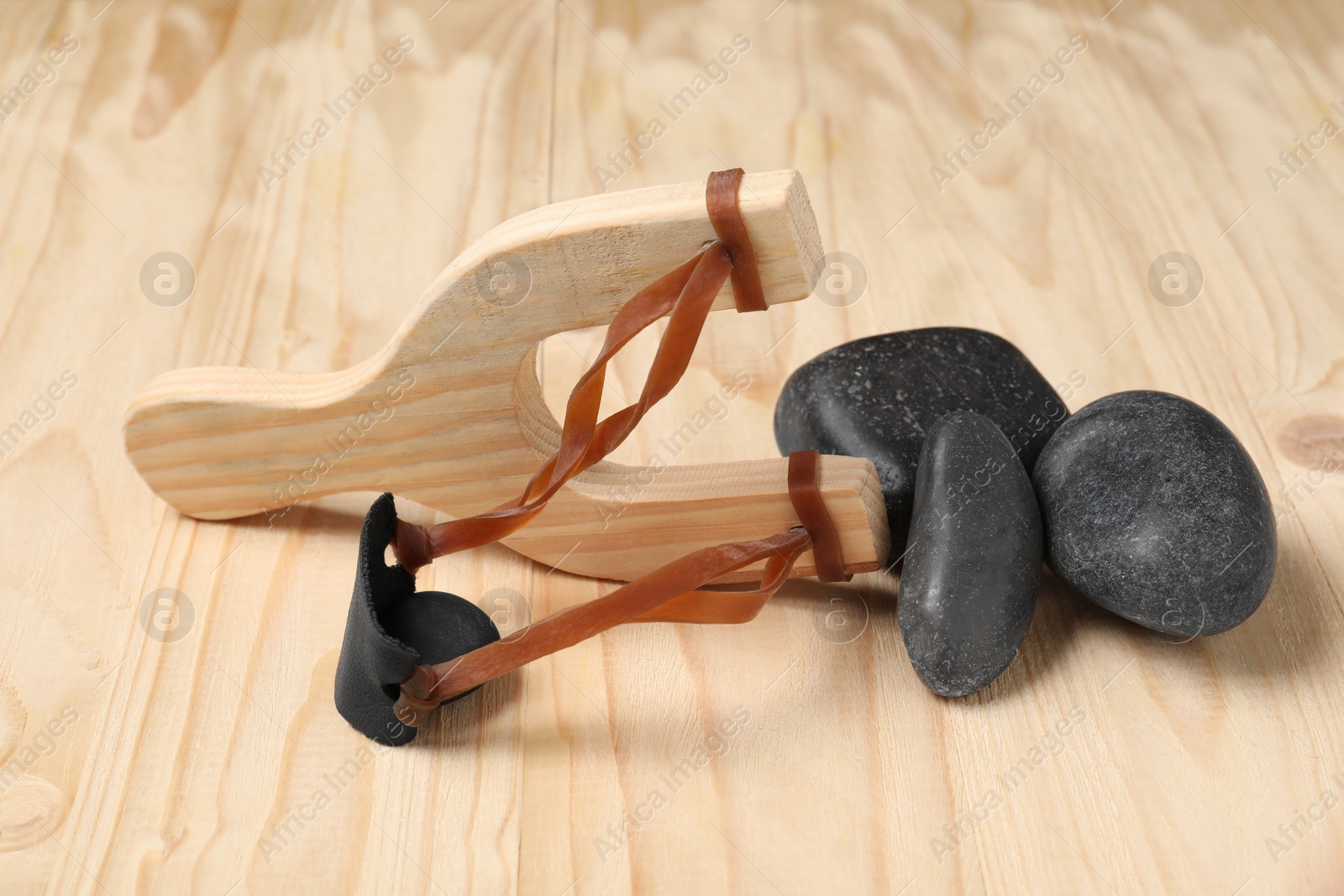 Photo of Slingshot with stones on wooden table, closeup