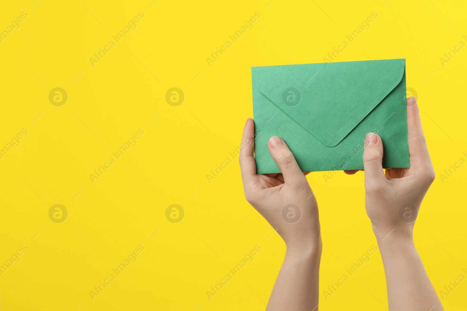 Photo of Woman holding green paper envelope on yellow background, closeup. Space for text