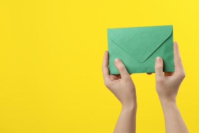 Photo of Woman holding green paper envelope on yellow background, closeup. Space for text