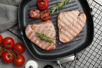 Photo of Delicious tuna steaks with rosemary and tomatoes on grey table, flat lay
